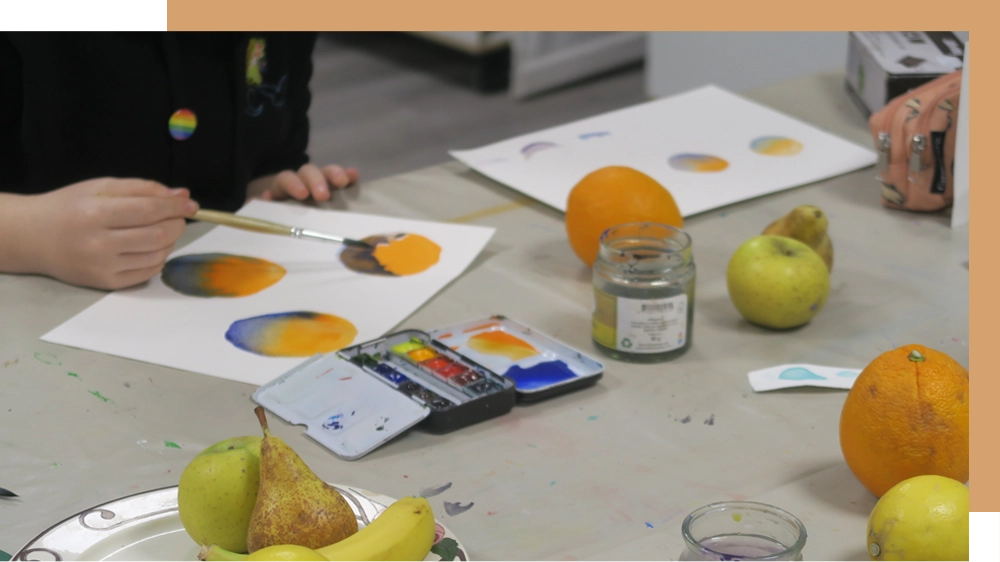 Une personne peignant sur une grande table avec des fruits posés dessus