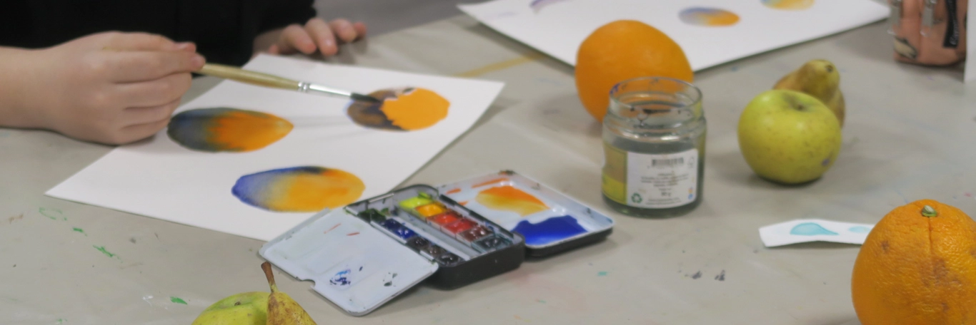 Une personne peignant sur une grande table avec des fruits posés dessus