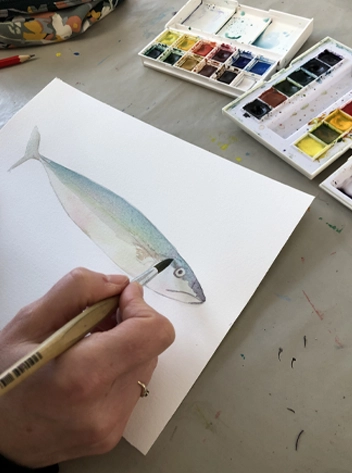 Feuille à dessiner avec une aquarelle en cours de réalisation, pinceau et godets de peinture visibles.